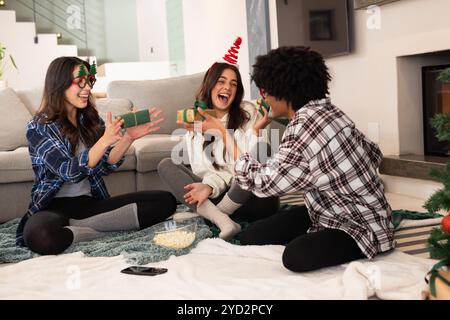 Amiche mutlirazziali che scambiano regali a casa durante le festività natalizie Foto Stock