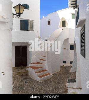 Binibeca Vell, Spagna, 24 gennaio 2024: Cortile con case bianche e scale nel centro del villaggio di Binibeca Vell, Europa Foto Stock