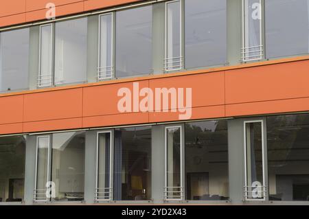 La luce del sole si riflette sulle grandi finestre di un moderno edificio di uffici caratterizzato da pannelli arancioni Foto Stock