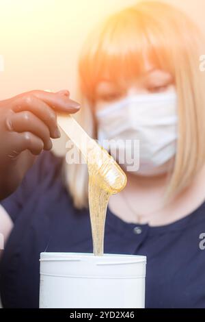 Mani femminili in guanti neri che contengono un recipiente di pasta per shugar pronto per la procedura di epilazione dello zucchero. Trattamenti spa. Beaut femminile Foto Stock