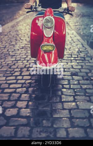 Un uomo in sella a Uno scooter o a Un ciclomotore lungo Una strada acciottolata a Roma, Italia, Europa Foto Stock