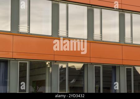 L'esterno di un moderno edificio di uffici mostra il design architettonico con rivestimento di colore arancione e grandi finestre che riflettono il cielo coperto Foto Stock
