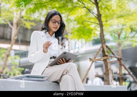 Giovani d'affari. Asiatico indiano donne lavoratrici ragazza intelligente con tablet verde parco all'aperto. Foto Stock