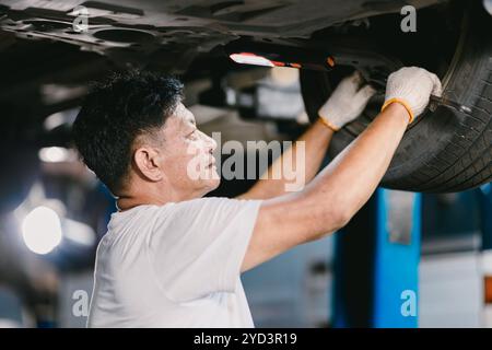 Happy Asian Mechanic Man Working Repair Vehicle in Car Service. Operatore che fissa il sistema di sospensioni sottovettura. Foto Stock