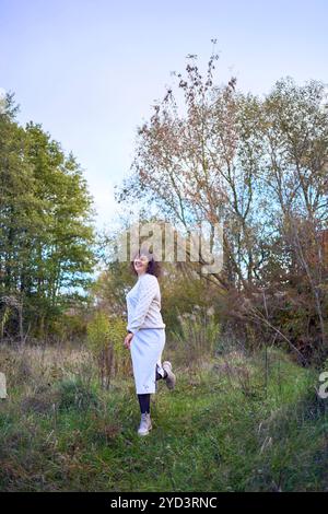 donna di mezza età con capelli ricci scuri in muta beige chiaro che gode della natura nella foresta autunnale Foto Stock