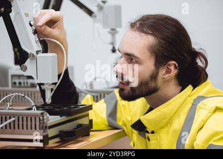 Formazione degli ingegneri maschi nel programma di robotica industriale in laboratori di ingegneria universitari apprendimento in aula braccio meccanico robot di assemblaggio. Foto Stock