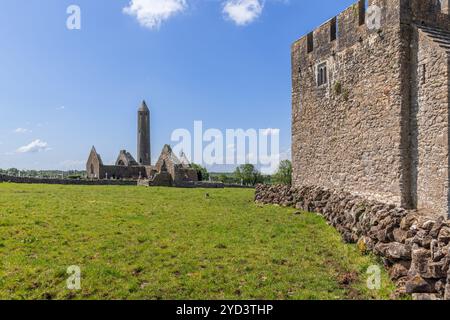 L'abbazia di Kilmacduagh nella contea di Galway, Irlanda, presenta una torre rotonda e rovine medievali adagiate su un cielo blu brillante Foto Stock