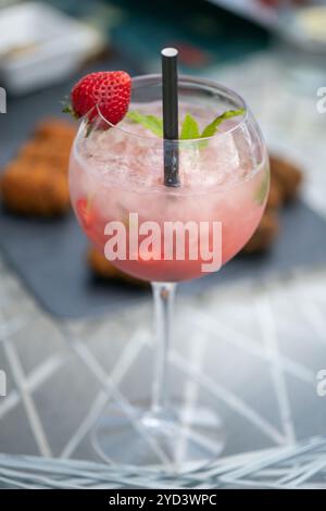 Un rinfrescante cocktail a base di fragole presentato in elegante bicchiere a stelo, bevanda alcolica servita con ghiaccio tritato e guarnita con foglie di menta Foto Stock
