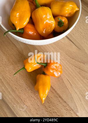 Peperoni habanero all'arancia su una superficie di legno con una ciotola bianca Foto Stock