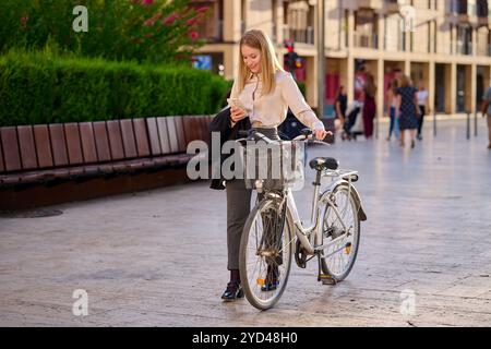 Giovane donna che controlla il telefono mentre sta accanto a una bicicletta Foto Stock