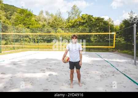 Giocatore di pallavolo in piedi su un campo di sabbia, tenendo in mano una palla e preparandosi per il gioco successivo durante un momento tranquillo in una partita di Beach volley all'aperto. Foto Stock