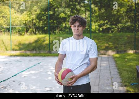 Giocatore di pallavolo in piedi su un campo di sabbia, tenendo in mano una palla e preparandosi per il gioco successivo durante un momento tranquillo in una partita di Beach volley all'aperto. Foto Stock