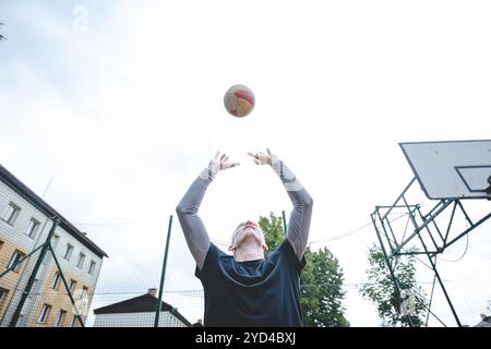 Giocatore di pallavolo che pratica l'impostazione della palla su un campo duro, concentrandosi sul controllo e la precisione durante una sessione di allenamento all'aperto. Una m calma e concentrata Foto Stock