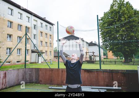 Giocatore di pallavolo che pratica l'impostazione della palla su un campo duro, concentrandosi sul controllo e la precisione durante una sessione di allenamento all'aperto. Una m calma e concentrata Foto Stock