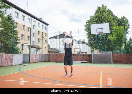 Giocatore di pallavolo che pratica l'impostazione della palla su un campo duro, concentrandosi sul controllo e la precisione durante una sessione di allenamento all'aperto. Una m calma e concentrata Foto Stock