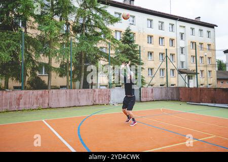 Giocatore di pallavolo che pratica l'impostazione della palla su un campo duro, concentrandosi sul controllo e la precisione durante una sessione di allenamento all'aperto. Una m calma e concentrata Foto Stock