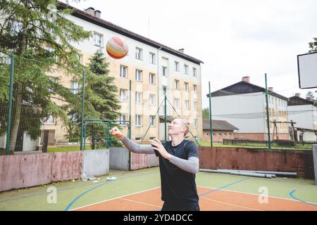 Giocatore di pallavolo che pratica l'impostazione della palla su un campo duro, concentrandosi sul controllo e la precisione durante una sessione di allenamento all'aperto. Una m calma e concentrata Foto Stock