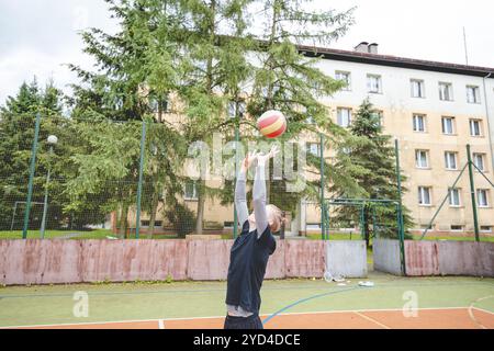 Giocatore di pallavolo che pratica l'impostazione della palla su un campo duro, concentrandosi sul controllo e la precisione durante una sessione di allenamento all'aperto. Una m calma e concentrata Foto Stock