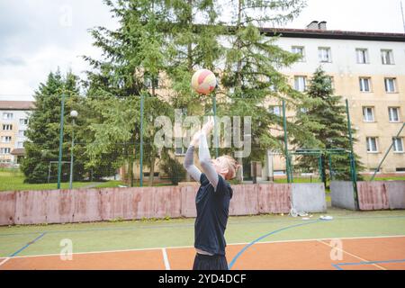 Giocatore di pallavolo che pratica l'impostazione della palla su un campo duro, concentrandosi sul controllo e la precisione durante una sessione di allenamento all'aperto. Una m calma e concentrata Foto Stock