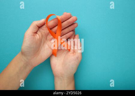 Mani con nastro arancione su sfondo blu. Consapevolezza del cancro renale, malattia di leucemia, consapevolezza del cancro della pelle, giornata mondiale del cancro. Assistenza sanitaria o Foto Stock