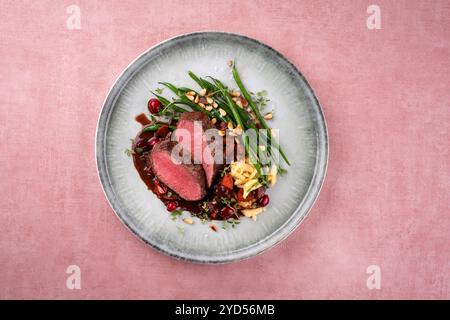 Tradizionale sella di filetto di cervo arrosto con spaetzle, fagioli e pinoli in salsa di selvaggina servita come vista dall'alto su un piatto di design nordico Foto Stock