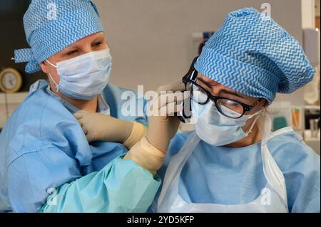 Due medici professionisti in scrub e maschere sono impegnati in una conversazione. Uno sta tenendo un telefono all'orecchio. Foto Stock