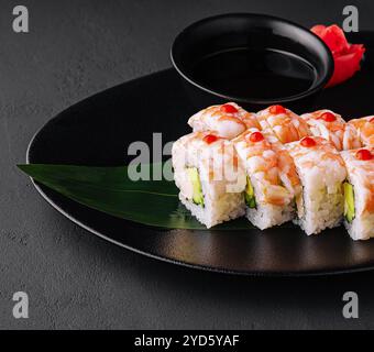 Rotolo di sushi ricoperto di carne di gamberi su piastra di ceramica nera Foto Stock