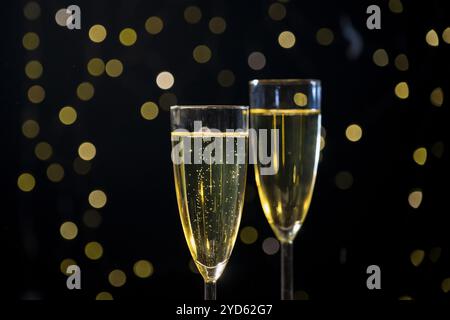 Champagne che bolle in due bicchieri mentre coriandoli dorati sfocati che cadono sullo sfondo con luci festose, primo piano. Concetto di festa per l'anno nuovo. Foto Stock