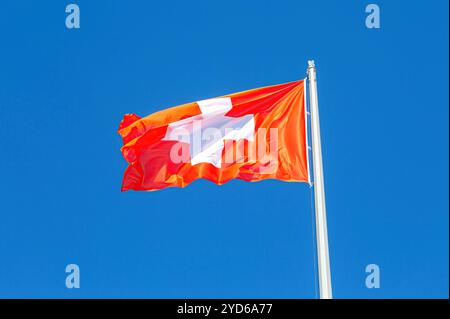 Bandiera della Svizzera che sventola nel vento contro un cielo blu Foto Stock