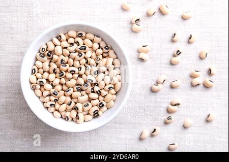 Piselli secchi dagli occhi neri in un recipiente bianco sopra il lino. Fagioli dagli occhi neri, o blackeye californiano, un legume di fagioli pallidi di medie dimensioni, con macchie nere. Foto Stock