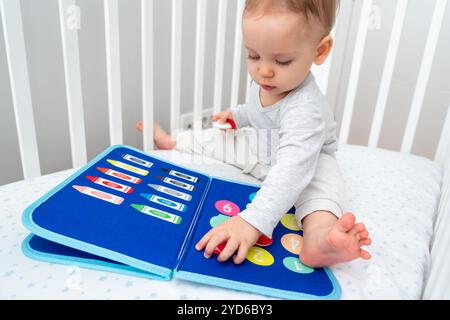 Una bambina che gioca con un libro affollato mentre si siede nella culla. Concetto di libri tranquilli e giocattoli educativi moderni Foto Stock