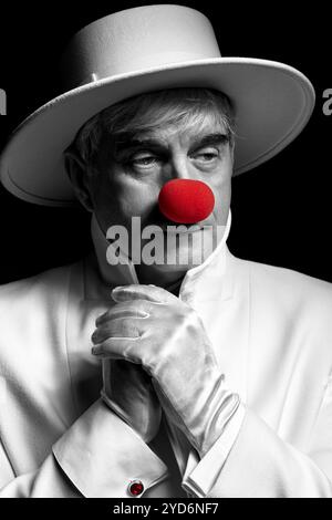 Primo piano, ritratto a colori selettivo del clown triste. Un uomo anziano con un cappotto bianco e un cappello. Foto Stock