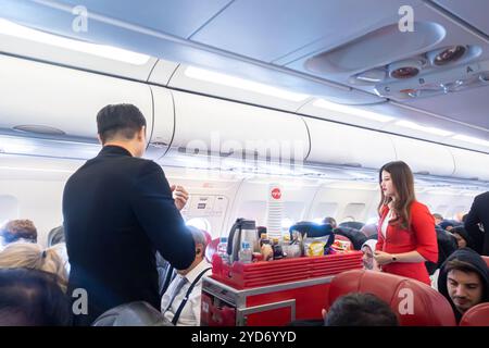 Assistenti di volo, uomini e donne, che servono cibo e bevande ai passeggeri dell'Airbus A320 operato da AirAsia Indonesia, Foto Stock