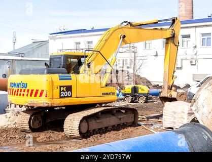Un escavatore sta lavorando in un cantiere per posare tubi di grande diametro in una trincea Foto Stock