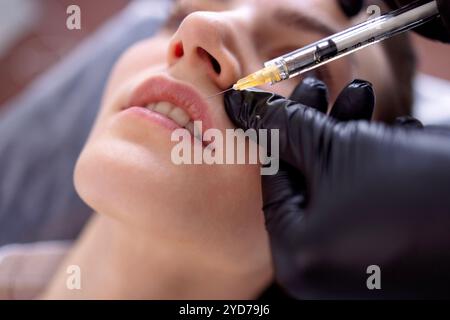 Iniezioni di bellezza. Cosmetologa donna in guanti neri fa un'iniezione Foto Stock