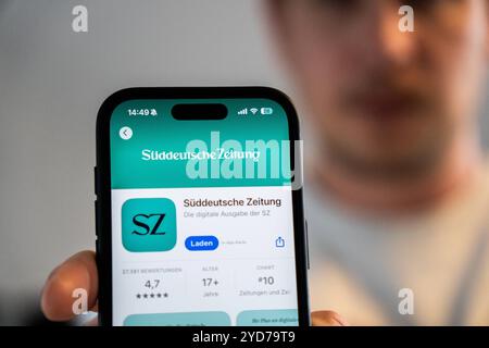 Baviera, Germania - 25 ottobre 2024: Un uomo possiede un iPhone con l'app Süddeutsche Zeitung SZ nell'Appstore. Immagine simbolica interruzione delle edizioni cartacee locali e chiusura degli uffici editoriali locali *** Ein Mann hält ein iPhone mit der App Süddeutsche Zeitung SZ im Appstore. Symbolbild Einstein der lokalen Printausgaben und schließung der Lokalredaktionen Foto Stock