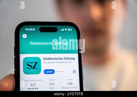 Baviera, Germania - 25 ottobre 2024: Un uomo possiede un iPhone con l'app Süddeutsche Zeitung SZ nell'Appstore. Immagine simbolica interruzione delle edizioni cartacee locali e chiusura degli uffici editoriali locali *** Ein Mann hält ein iPhone mit der App Süddeutsche Zeitung SZ im Appstore. Symbolbild Einstein der lokalen Printausgaben und schließung der Lokalredaktionen Foto Stock