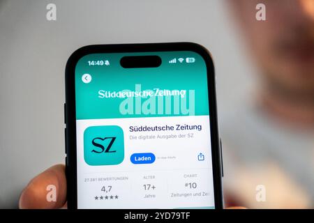 Baviera, Germania - 25 ottobre 2024: Un uomo possiede un iPhone con l'app Süddeutsche Zeitung SZ nell'Appstore. Immagine simbolica interruzione delle edizioni cartacee locali e chiusura degli uffici editoriali locali *** Ein Mann hält ein iPhone mit der App Süddeutsche Zeitung SZ im Appstore. Symbolbild Einstein der lokalen Printausgaben und schließung der Lokalredaktionen Foto Stock