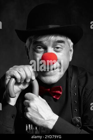 Ritratto a colori selettivo di clown ridendo su uno sfondo scuro appoggiato sul manico di un ombrello. Foto Stock