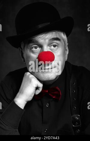 Spettacolare ritratto a colori selettivo di un pagliaccio triste su sfondo scuro. Mano vicino alla faccia. Foto Stock