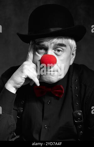 Spettacolare ritratto a colori selettivo di un pagliaccio triste su sfondo scuro. Mano vicino alla faccia. Foto Stock