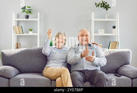Ritratto di una vecchia coppia felice dai capelli grigi che guarda la partita di calcio in TV insieme a casa. Foto Stock