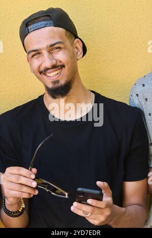 Un sorprendente primo piano che cattura il sorriso radioso di un adolescente sudanese, completato da un mento e da un elegante berretto tramite smartphone Foto Stock