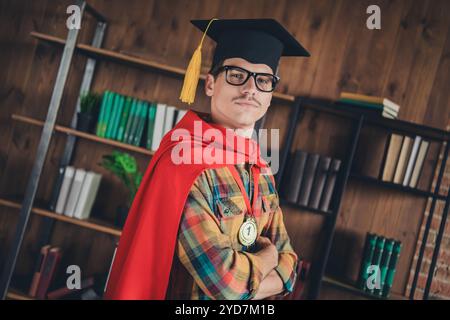 Foto di un giovane uomo bello e sicuro di sé indossa una camicia a quadri cappello rosso mantello che si è diplomato al diploma di laurea magistrale Foto Stock