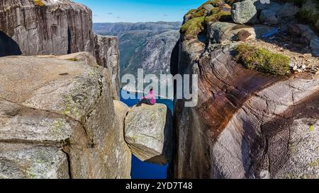 Un escursionista solitario siede ai margini di Kjeragbolten, Norvegia, una famosa scogliera in Norvegia, che si affaccia su un fiordo mozzafiato Foto Stock