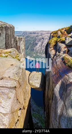 Un escursionista solitario si erge sul bordo del Kjeragbolten, una scogliera in Norvegia, che si affaccia sul vasto paesaggio norvegese Foto Stock