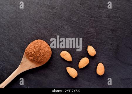 Cucchiaio di cacao in polvere e mandorle su sfondo scuro Foto Stock