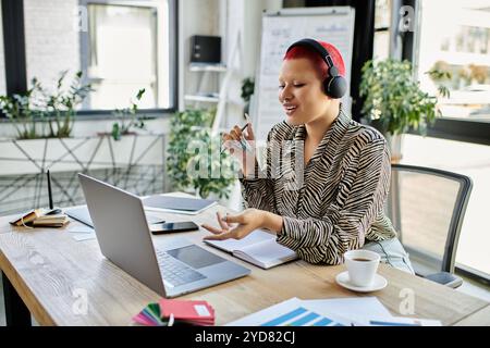 La donna calva con una camicia fantasia parla entusiasticamente mentre lavora alla sua scrivania. Foto Stock