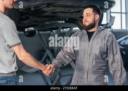 Il meccanico agita le mani con il proprietario dell'auto nel garage dell'officina. Concetto di servizi auto Foto Stock