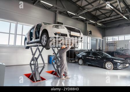 Meccanico che ripara l'automobile sull'ascensore in officina meccanica o garage, all'interno dell'officina di riparazione auto Foto Stock